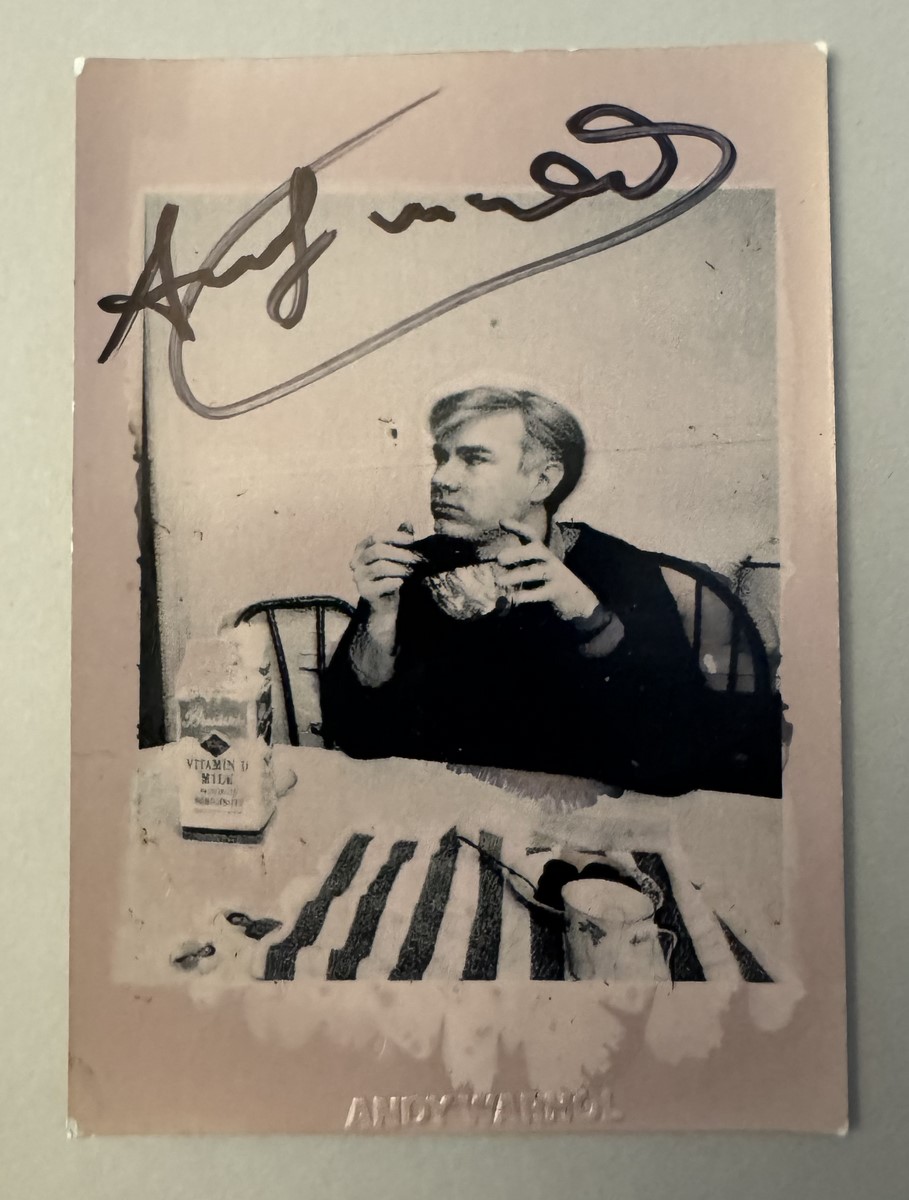 Andy WARHOL (1928-1987), Attribué à. Photographie argentique en noir et blanc, représentant Andy Warhol au déjeuner. Signé au marqueur. Tampon de la signature « Andy Warhol » au dos de la photographie. Timbre sec en creux Andy Warhol.