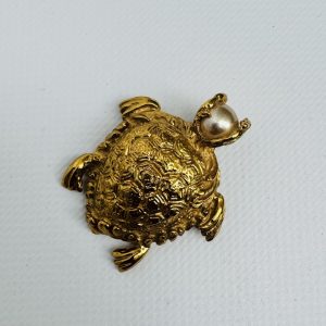 YVES SAINT LAURENT. Broche-pendentif en métal doré, ciselé et perle d’imitation, figurant une tortue. Signé.