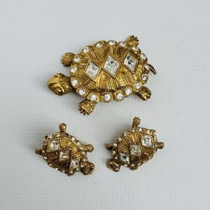 CHRISTIAN DIOR - Une broche et une paire de boucles d’oreille en métal doré et strass figurant une tortue. Signé.4,8 x 4,5 cm – 3,8 x 3,6 cm