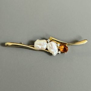 BROCHE en or jaune 18k (750 millièmes) ornée sur la partie centrale de deux perles baroques, petits diamants et un grenat.