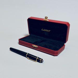 CARTIER.  Stylo Roller-Ball de la collection Diabolo, résine noire, attributs plaqués or.  Cabochon saphir au sommet du capuchon. Signé. Dans son coffret d’origine. Poids brut : 39 gr.