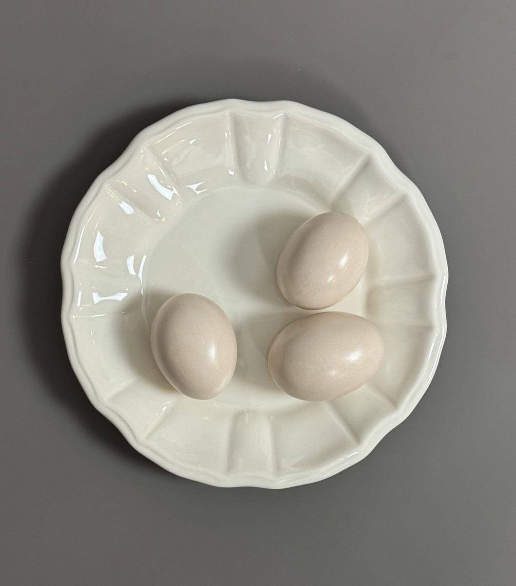 DIOR. Assiette décorative en faïence écrue à motif 3 œufs en trompe-l’œil.