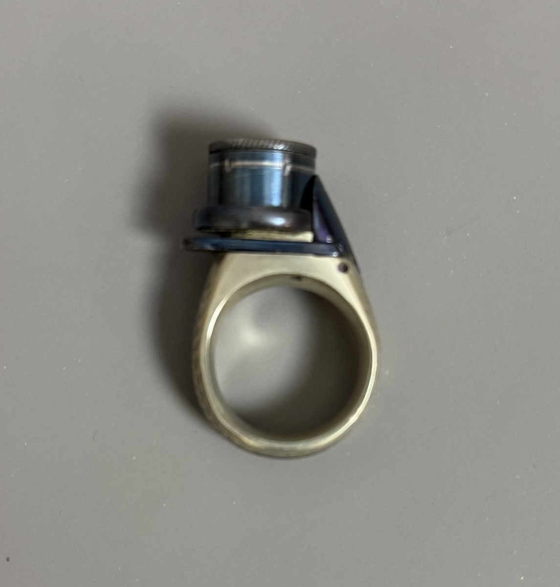 BAGUE RÉVOLVER, « le petit Protector », à broche, 6 coups, calibre 4 mm. Barillet bleu, guilloché sur le bord pour être tourné à la main. Détente latérale. Anneau en maillechort gravé de feuillages et marqué « LE PETIT PROTECTOR » XXe siècle. Dans son coffret en cuir décoré au petit fer, avec plaque en argent gravée « Le petit protector », garni à l’intérieur de velours. Avec sa boîte d’origine (6,7 x 8,2 , 2 cm) , 6 balles de plomb et un tournevis. Complet. - Image 3