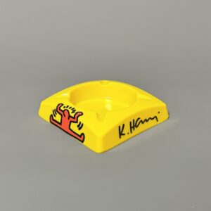 Keith HARING (1958-1990), D’Après.  Cendrier en plastique jaune. Signé au marqueur. Longueur : 11,5 cm- Largeur : 11,5 Hauteur : 3 cm