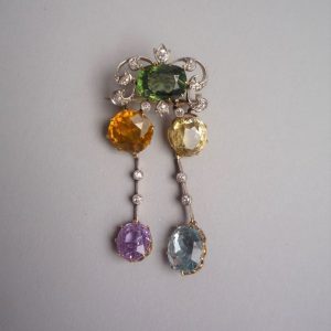 BROCHE en or jaune 14K (585°/00) stylisée ornées de saphirs de couleurs, d’une topaze et diamants. Peut se porter en pendentif. En partie début du XXème siècle. Poids brut : 11,4 g.
