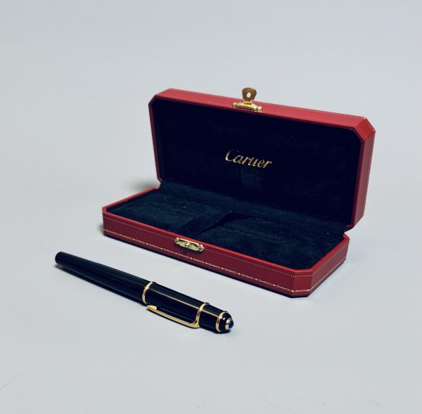 CARTIER.  Stylo Roller-Ball de la collection Diabolo, résine noire, attributs plaqués or.  Cabochon saphir au sommet du capuchon. Signé. Dans son coffret d’origine. Poids brut : 39 gr.