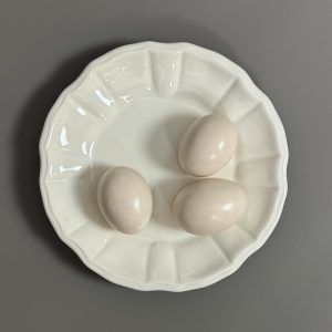 DIOR.   Assiette décorative en faïence écrue à motif 3 œufs en trompe-l’œil.